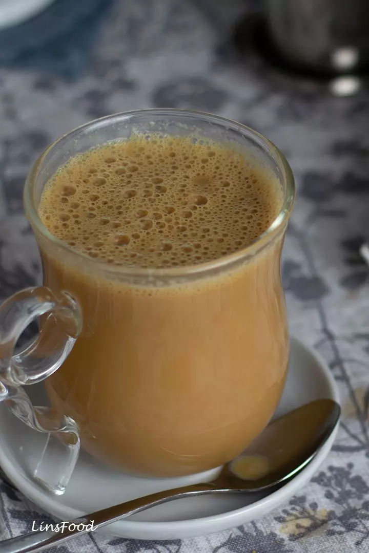 Close-up of a glass of Teh Tarik with froth on top, placed on a table.