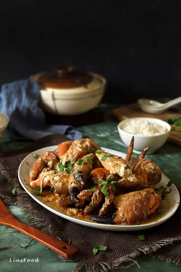 Singapore chilli crab in a oval plate with a bowl of rice and claypot in background
