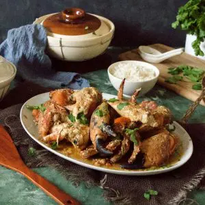 Singapore chilli crab in a oval plate with a bowl of rice and claypot in background
