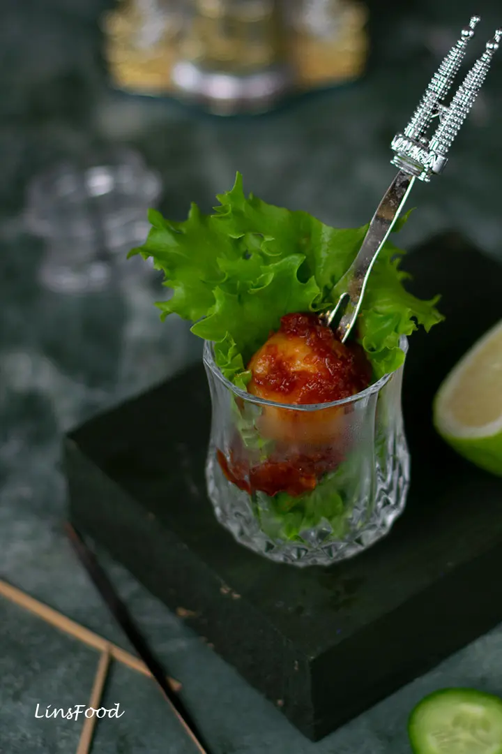 fishballs covered in spicy red sauce in small crystal shot glass with lettuce