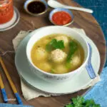 bowl of prawn ball soup with chilli and soy sauce in little bowls