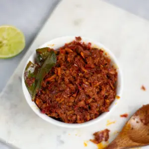sambal hae bee, spicy dried shrimp condiment in a white bowl with kaffir lime leaf