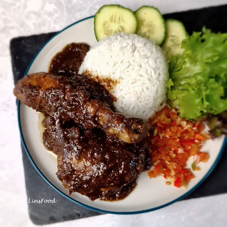 A plate of Ayam Sioh, a traditional Nyonya chicken stew with tamarind and coriander, served with jasmine rice, sambal and salad on a black slate
