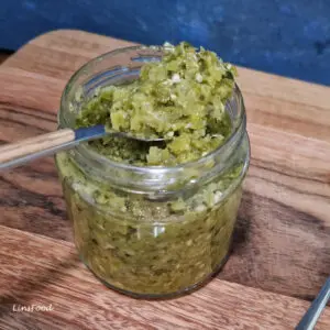 Sambal ijo green chilli sambal from Indonesia in a glass jar with a spoon on a wooden board, a spicy condiment made with green chillies and tomatoes.