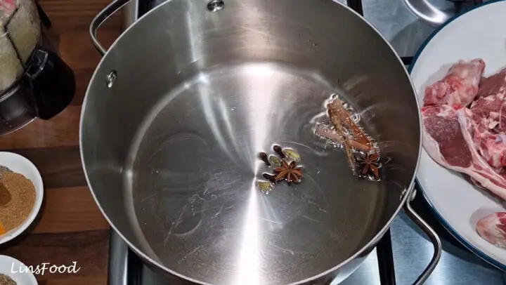 Whole spices frying in oil for sup kambing, with lamb and onion paste ready beside the pan.