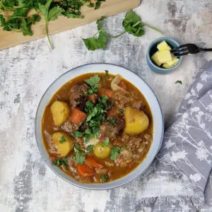 Eurasian beef smore (beef stew) in a light blue bowl topped with a knob of butter and scattered coriander leaves.