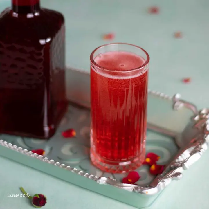 Easy rose syrup drink in a Collins glass with a bottle of homemade rose syrup on a green tray