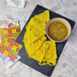 Roti jala folded on a black slate board beside a bowl of curry.