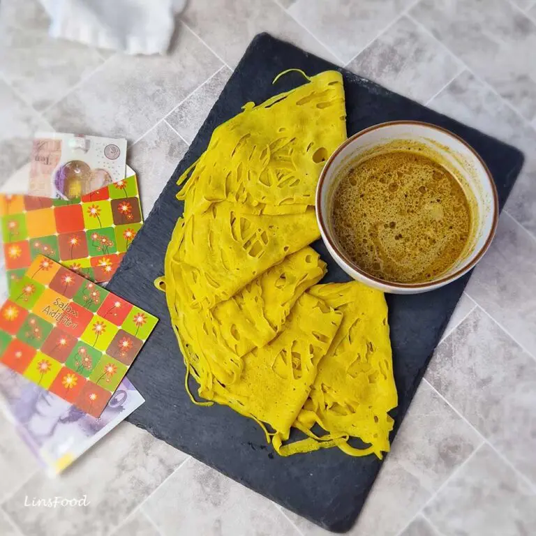 Roti jala folded on a black slate board beside a bowl of curry.