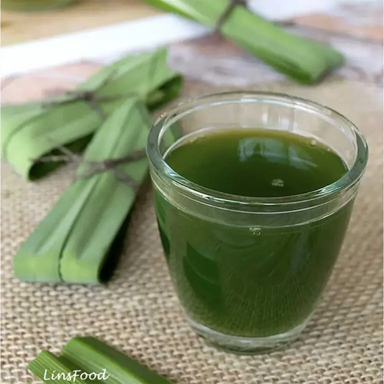 Fresh pandan juice in a glass with tied pandan leaves in the background