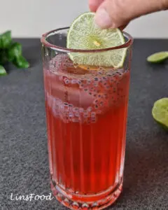 A fresh lime slice being added to a glass of sirap limau selasih.