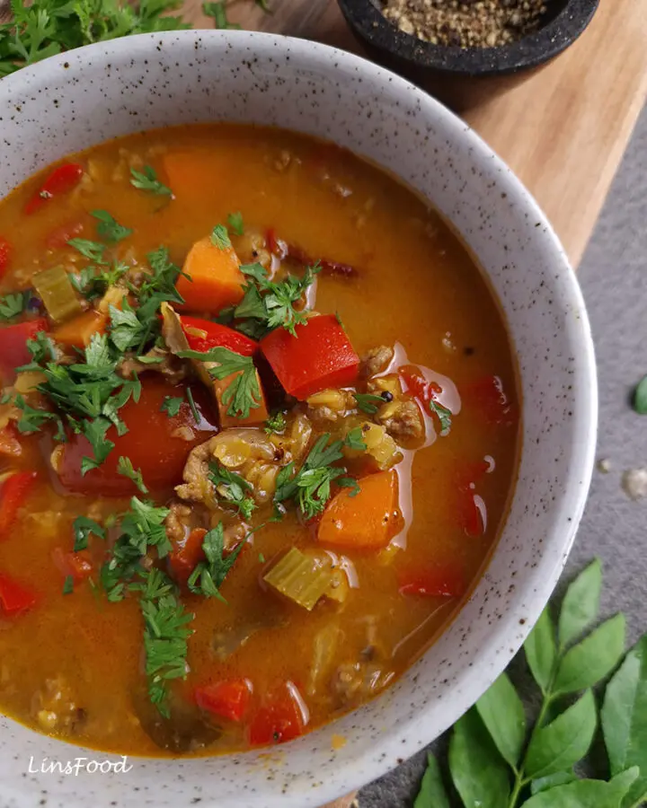 Close-up of mulligatawny soup with minced beef, red lentils, carrots, celery and red capsicum, topped with coriander.
