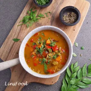 Overhead bowl of beef mulligatawny soup on a wooden board with coriander, curry leaves and freshly ground black pepper.