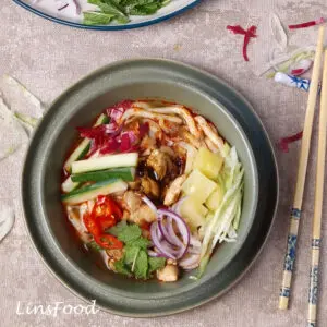 Overhead view of Penang asam laksa with mackerel, thick noodles, pineapple, cucumber, onion, mint and bunga kantan