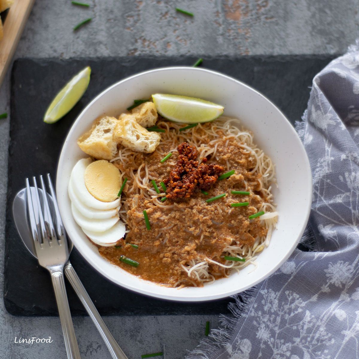 white bowl with noodles in gravy, topped with sliced eggs, tofu, lime and chilli paste, mees siam kuah