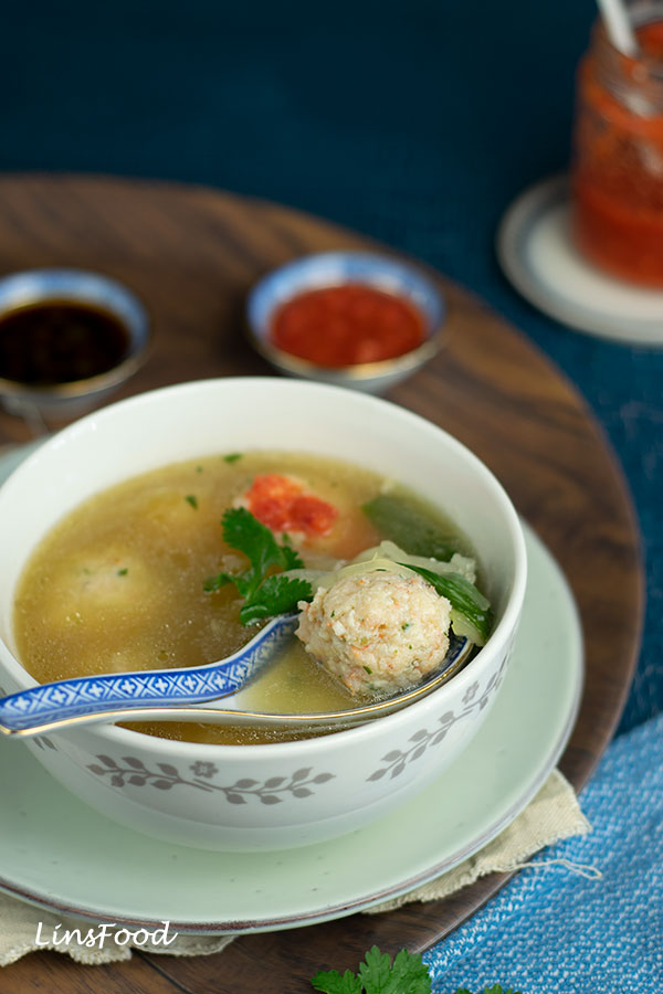 bowl of prawn ball soup with chilli and soy sauce in little bowls