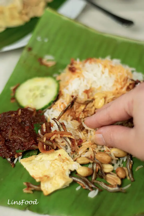 fingers scooping up nasi lemak with sambal, ikan bilis and egg