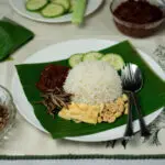 coconut rice, nasi lemak on pandan leaf surrounded by sambal, omelette, anchovies and peanuts, cucumbers