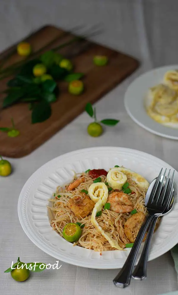 Mee Siam Goreng, fried malaysian bee hoon on a white plate topped with omelette strips and calamansi limes