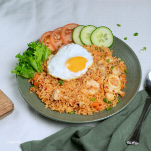 nasi goreng USA on a green plate with fried egg and cucumbers and tomatoes