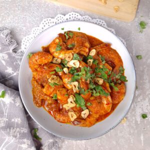 prawn sambal bostador, spicy Eurasian recipe in a light blue bowl, with fried garlic and and coriander leaves on a wooden board