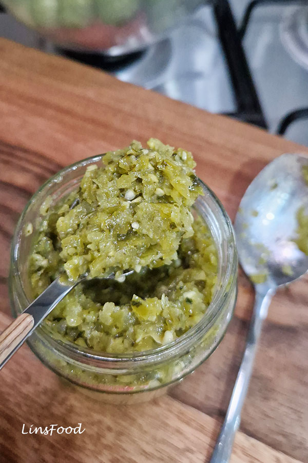 Sambal ijo green chilli sambal from Indonesia in a glass jar with a spoon on a wooden board, a spicy condiment made with green chillies and tomatoes.