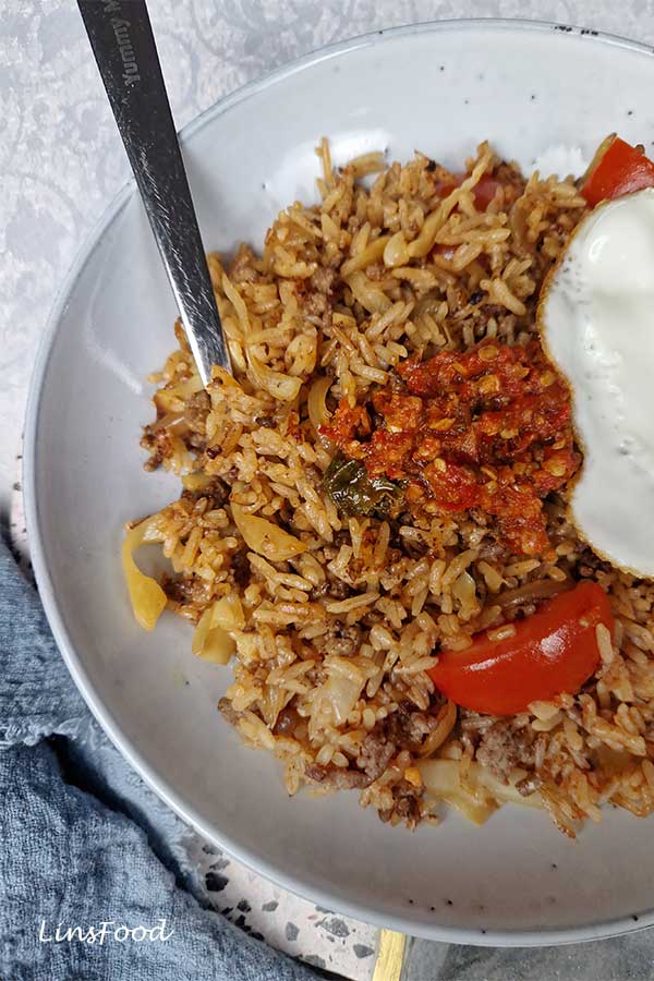 Nasi goreng sambal with beef, fried egg and tomato wedge on a rustic plate.