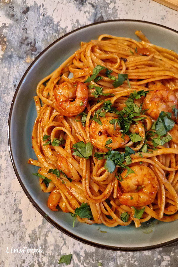 Close-up of prawn sambal pasta in a pan with garlic and onion.