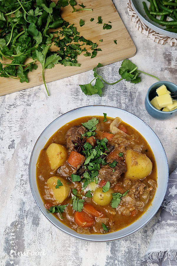 Comforting Eurasian beef stew in a light blue bowl, garnished with butter and coriander leaves.
