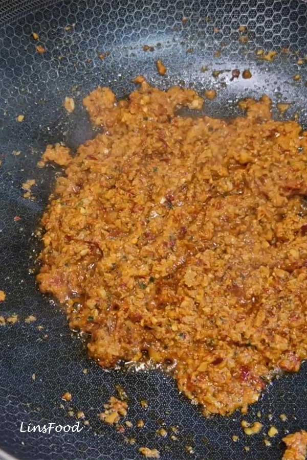 Oil splitting stage while frying a spice paste in a wide pan, glossy curry paste with oil separating around the edges.