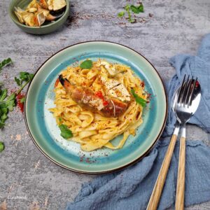 Singapore-style chilli crab linguine piled on a blue-green plate, glossy red chilli crab sauce with flakes of crab meat and coriander.