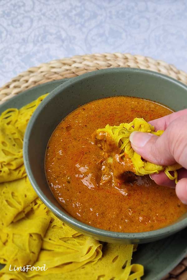 Alt Text
Hand dipping folded roti jala into a bowl of curry.