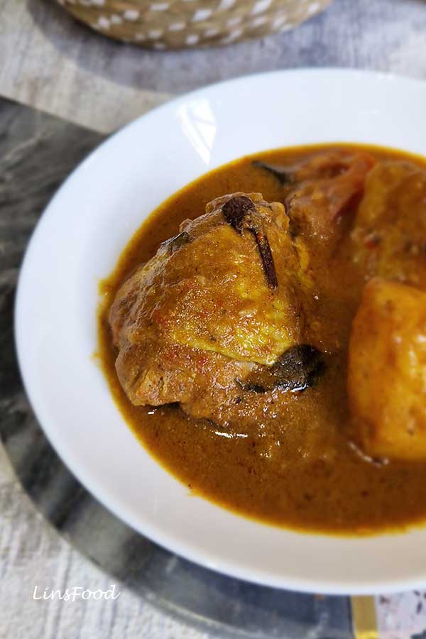 Close-up of chicken thigh in Kari Ayam, a Singaporean/Malaysian chicken curry made with curry powder, coconut milk, tomatoes and curry leaves.