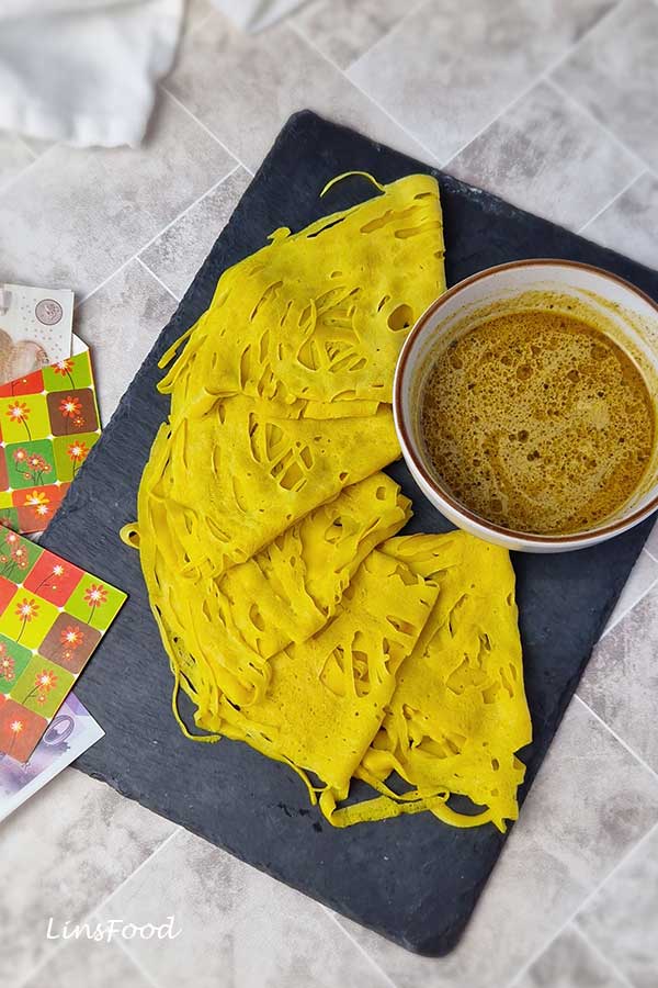 Folded roti jala on a slate board with a bowl of curry, photographed from above.