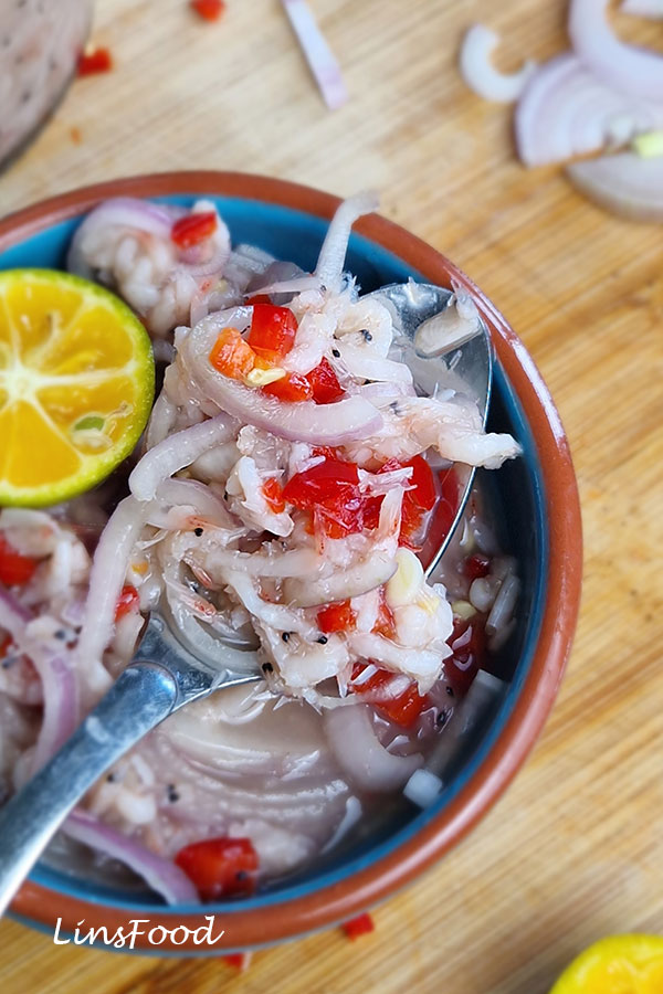 Close-up of sambal cincalok on a spoon with fermented shrimp, sliced shallots and chopped red chilli.