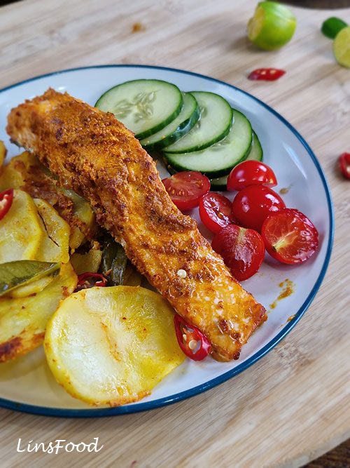 Close-up of ikan bakar-inspired salmon with turmeric potatoes, cucumber, tomatoes and lime.