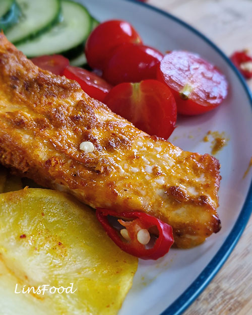 Close-up of sambal salmon with turmeric potatoes, cucumber, tomatoes and sliced red chilli.