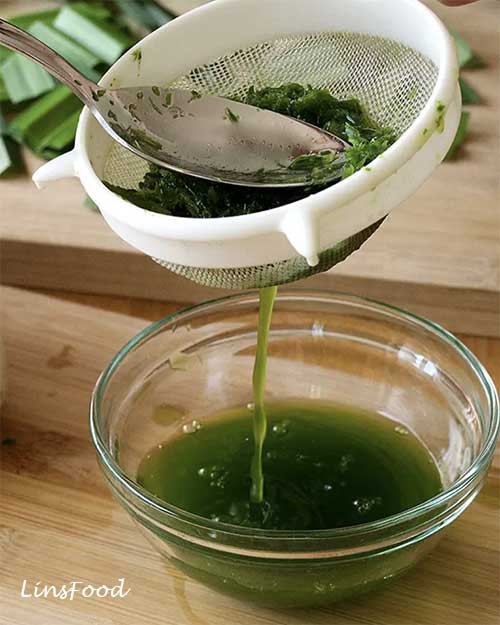 Fresh pandan juice being strained through a sieve into a glass bowl