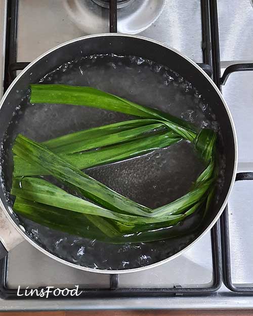 Whole pandan leaves simmering in hot water in a saucepan