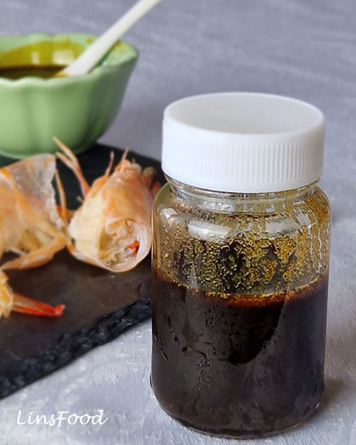 Homemade petis udang stored in a small lidded jar with prawn shells behind